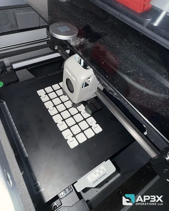 Inside the X1 Carbon: a black build plate holding rows of white infinity cube pieces, with the toolhead parked above them.