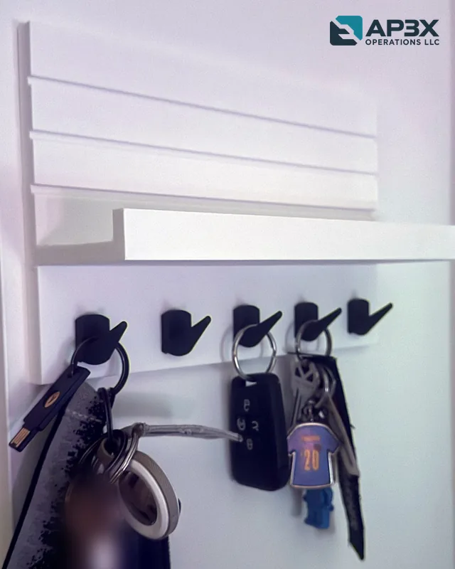 White 3D-printed wall key rack with five black hooks and a shelf, holding several sets of keys.